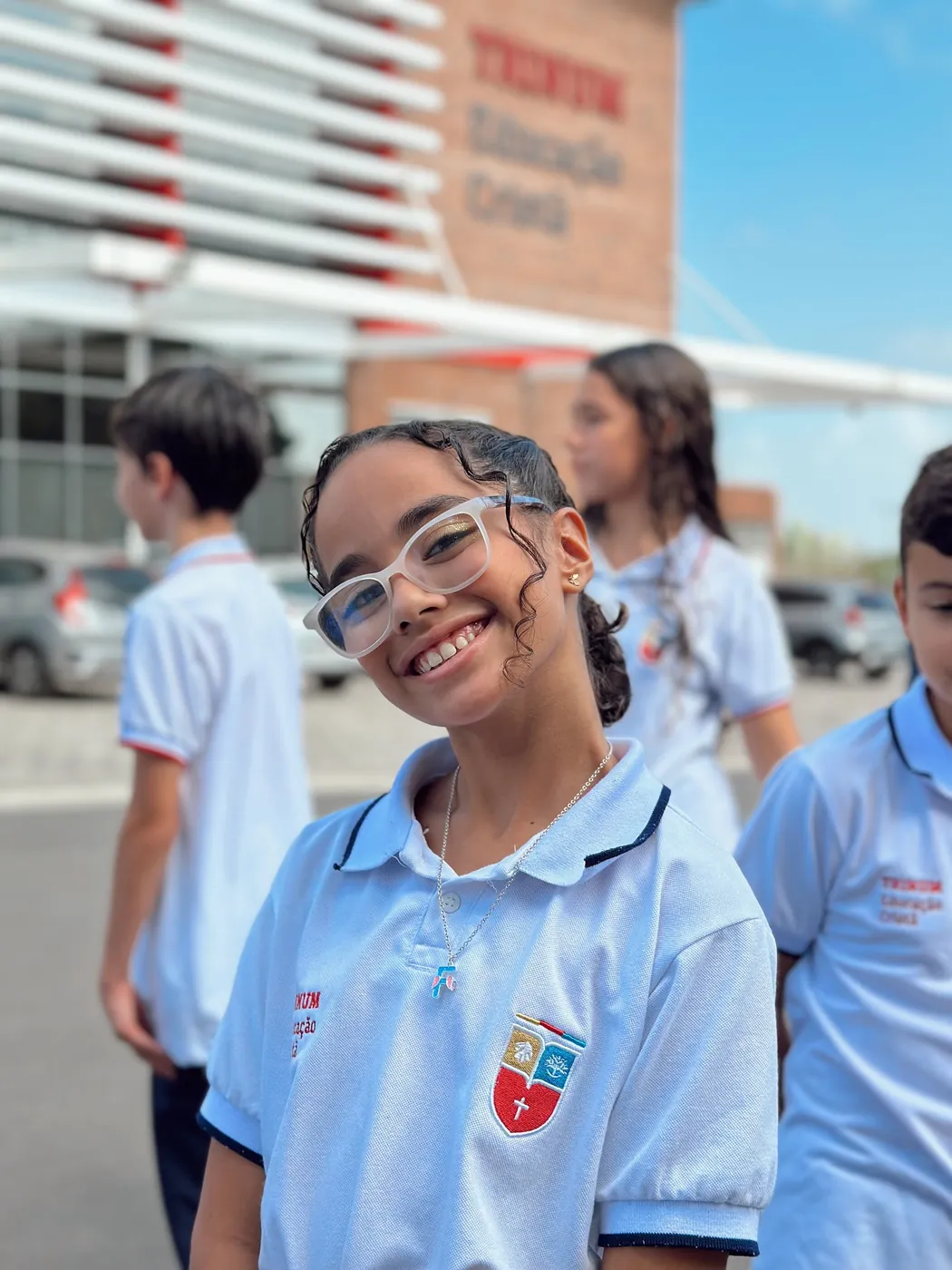 Aluna sorrindo no pátio diante da fachada da escola