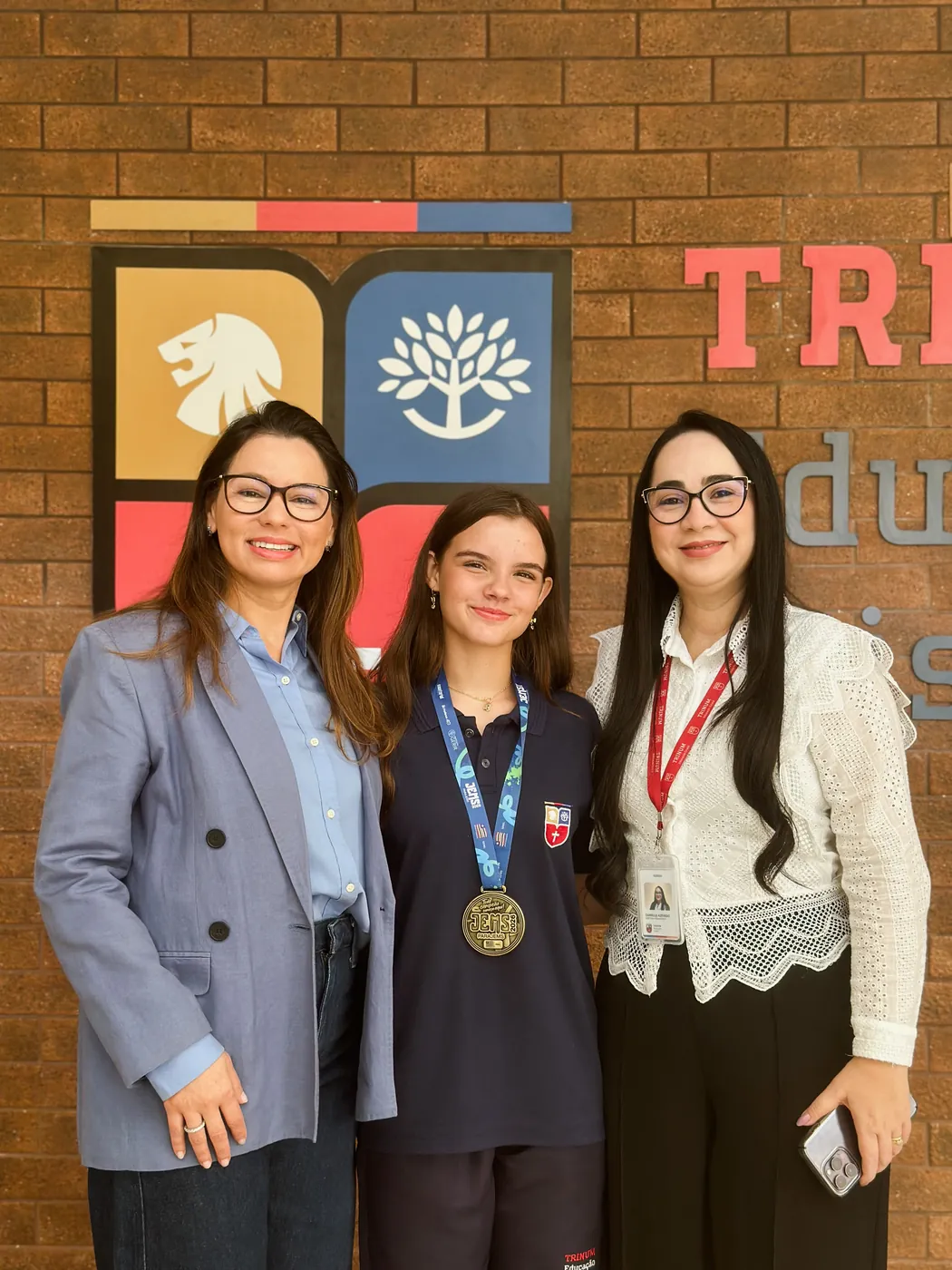 Aluna medalhista ao lado de duas educadoras